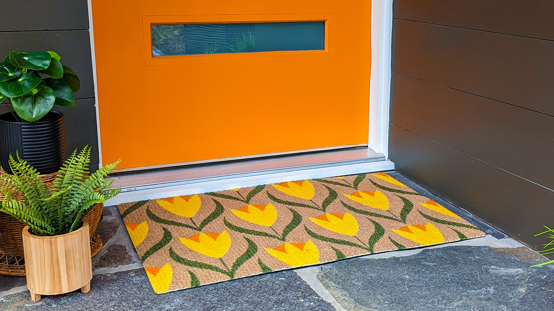 Bright and multi-colored cute doormat placed in front of orange midcentury modern door.
