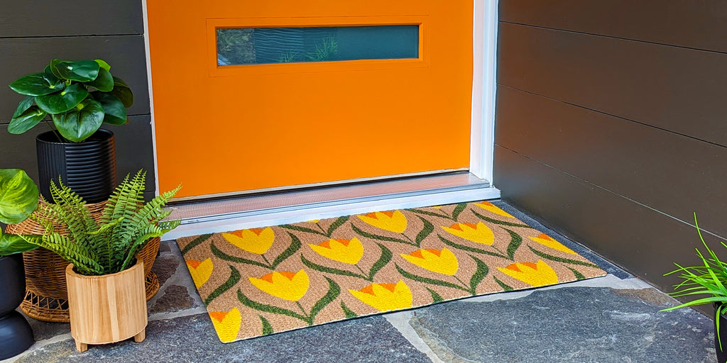 Bright and multi-colored cute doormat placed in front of orange midcentury modern door.