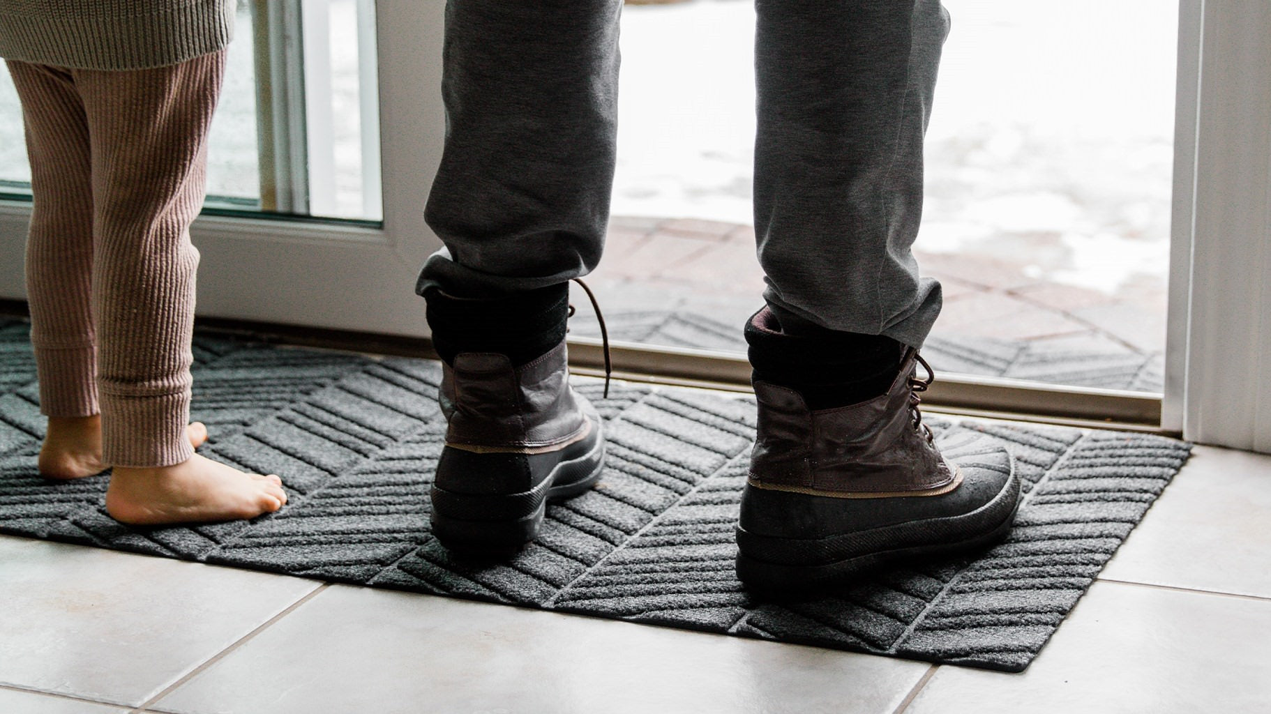 Small child standing on durable all-weather WaterHog outdoor doormat placed at sliding door to capture snow.