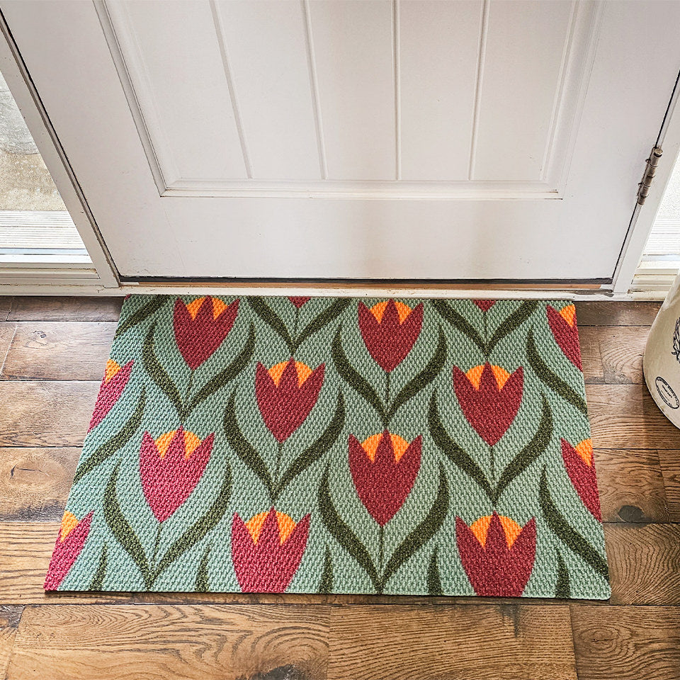 Sage and berry colored Buttercups single door doormat in front of a shut door.