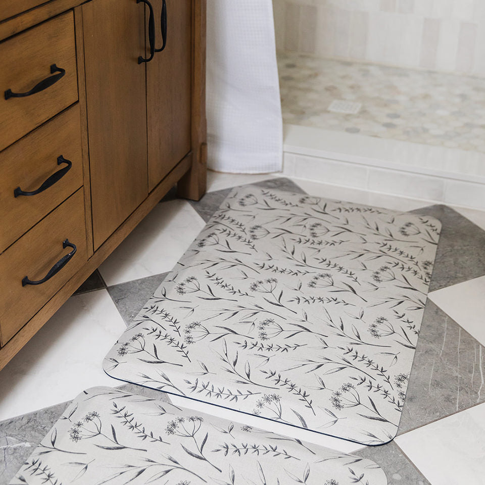 Floral Botanical Happy Feet bath mats with grey flowers on an off-white background on a wipeable surface.