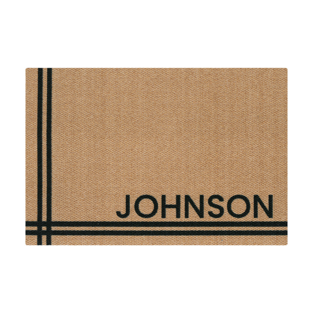 Isolated tan doormat personalized with black-colored 'JOGNSON' text in all caps in the lower right corner with two pairs of # meeting in the lower left corner