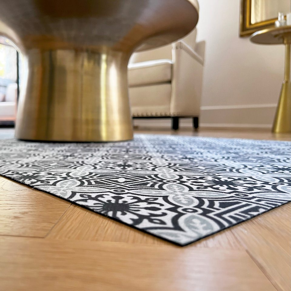 Beautiful low-profile Un-Rug in classic porto geometric architectural design in navy and sea salt green being used as a decorative area rug with coffee table on top.