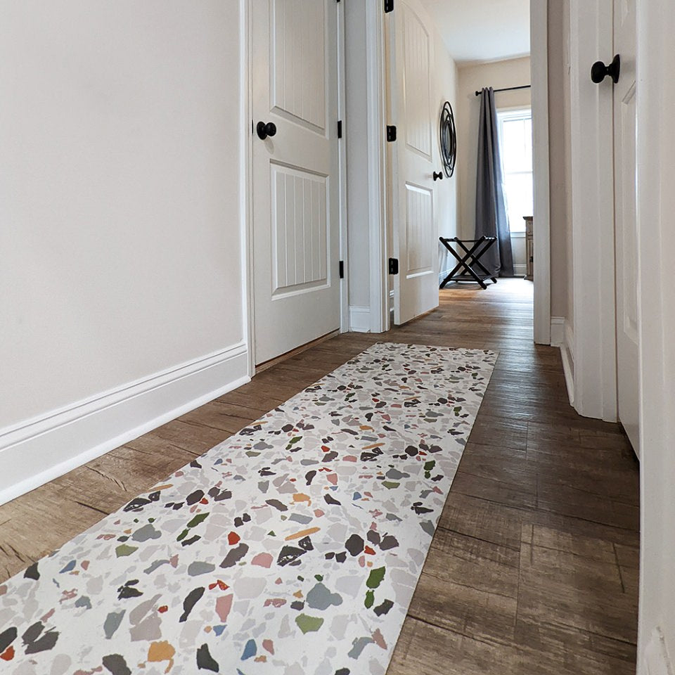 Overhead view of Un-Rug low-profile decorative accent mat in a rectangular runner size in a light neutral background and terazzo pattern in multi colors being used in a hallway.