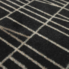 Close-up of the Maxcent Biblioteca area mat in charcoal, showing the soft carpeted surface with a modern beige line pattern over a deep charcoal background. The textured fibers provide a durable, comfortable feel underfoot.