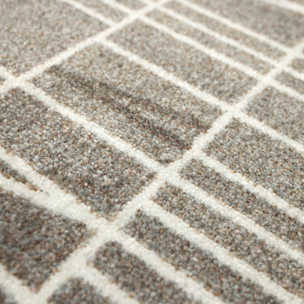 Close-up of the Maxcent Biblioteca area mat in Light Greige, showing the textured carpeted surface with a modern grid and angle pattern. The tight, low-pile weave offers durability and comfort underfoot.