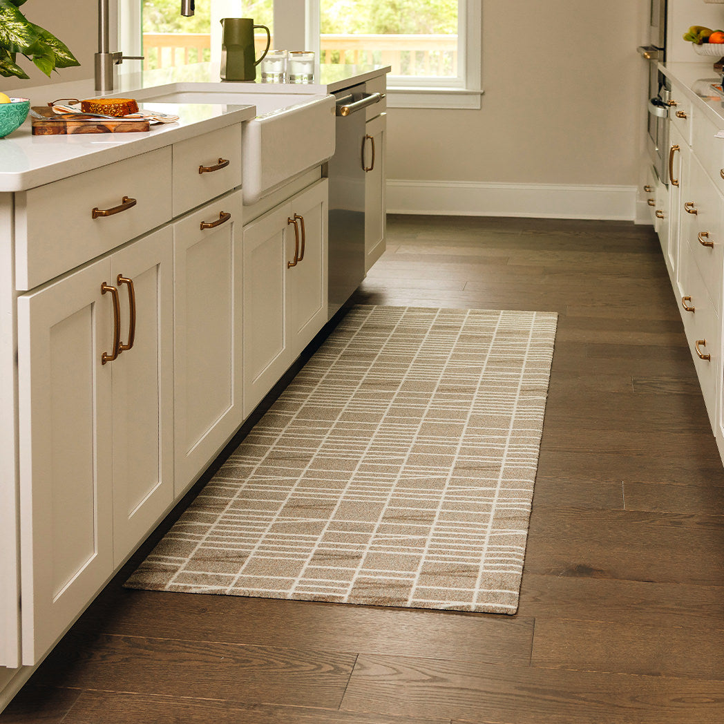 Maxcent Biblioteca runner mat in Light Greige – placed in a galley-style kitchen on dark wood floors. The rug features a beige-gray background with off-white grid lines, creating a clean, modern look. Its soft carpeted surface and non-slip backing offer comfort and stability in high-use areas like in front of a sink or stove.