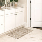 Maxcent Biblioteca area mat in Light Greige, small size – placed in front of a white bathroom vanity on marble tile flooring. The modern grid pattern in white on a light grey background and low-profile design offer a clean, contemporary look, while the non-slip backing helps keep the mat in place.