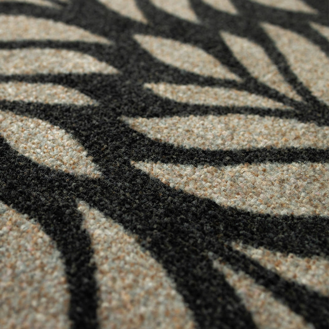 Close-up of the Maxcent Botanica mat in Space Grey, showing the textured carpeted surface with a bold black leaf pattern over a soft gray base. The detailed weave provides a comfortable feel underfoot and enhances the visual depth of the design.