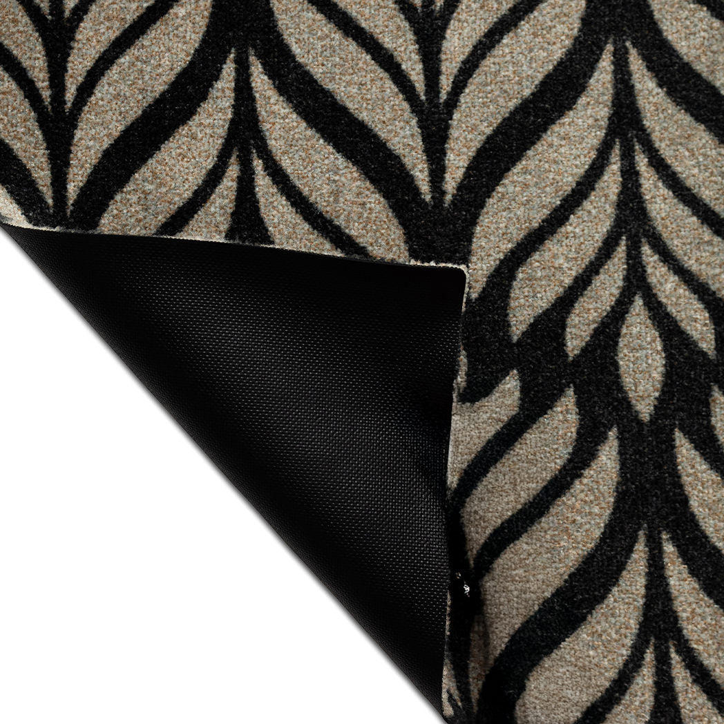 Corner of the Maxcent Botanica mat in Space Grey lifted to reveal the textured black rubber backing. The carpeted top features a soft gray leaf pattern over a deep black background, blending bold contrast with a non-slip design for stability on hard floors.