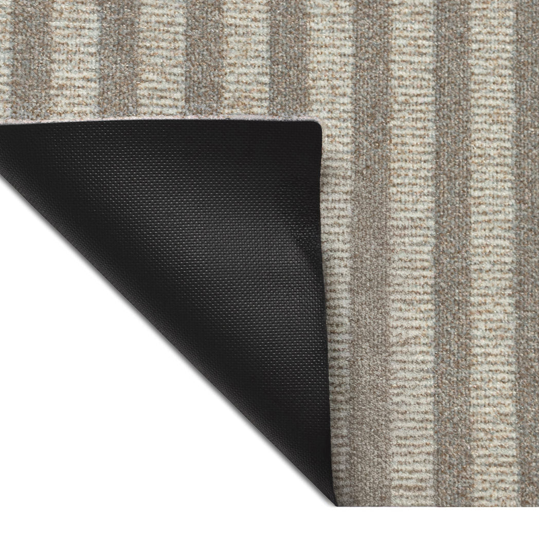 Corner detail of the Maxcent Classic Stripe mat showing its non-slip rubber backing. The surface features alternating narrow stripes in soft beige and grey tones, offering a simple, neutral look with built-in grip for added stability.