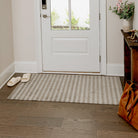 Maxcent Classic Stripe mat in medium size placed by a front entryway. The vertical striped design in soft beige and grey tones blends effortlessly with the neutral decor, offering a clean, welcoming touch while helping to trap dirt and moisture from shoes.