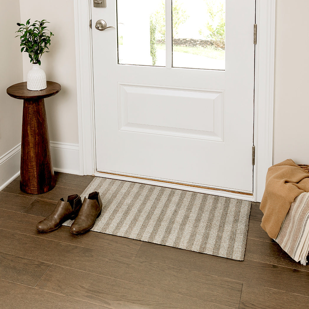 Maxcent Classic Stripe mat in a small size placed at a front door entryway. The mat’s soft beige and grey striped pattern complements the light wood flooring, offering a clean, neutral accent while helping catch dirt and moisture from shoes.