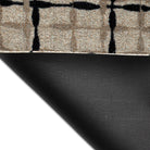 Corner of the Maxcent Heritage Tweed mat in Greige & Inkwell lifted to reveal the textured black rubber backing. The carpeted top features a warm beige/grey background with a bold black crosshatch pattern, combining slip resistance with a modern woven look.