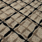 Close-up of the Maxcent Heritage Tweed mat in Greige & Inkwell, showing a textured carpeted surface with a warm beige/grey background and a black crosshatch pattern. The subtle weave and contrasting lines create a sophisticated, modern grid effect