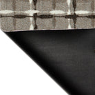 Corner of the Maxcent Heritage Tweed mat in Light Greige lifted to reveal the textured black rubber backing. The carpeted top displays a warm beige/grey background with a crosshatch pattern in dark brown and off-white, combining comfort and slip-resistant functionality.