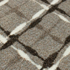 Close-up of the Maxcent Heritage Tweed mat in Light Greige, showing a warm beige/grey background with a crosshatch pattern in dark brown and off-white. The textured carpeted surface adds depth and softness, giving the design a refined, woven look.
