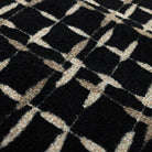 Close-up of the Maxcent Heritage Tweed area rug in Inkwell, showing a textured carpeted surface with a black background and a crosshatch design in light gray and tan. The tightly woven fibers and layered pattern add depth and visual interest.