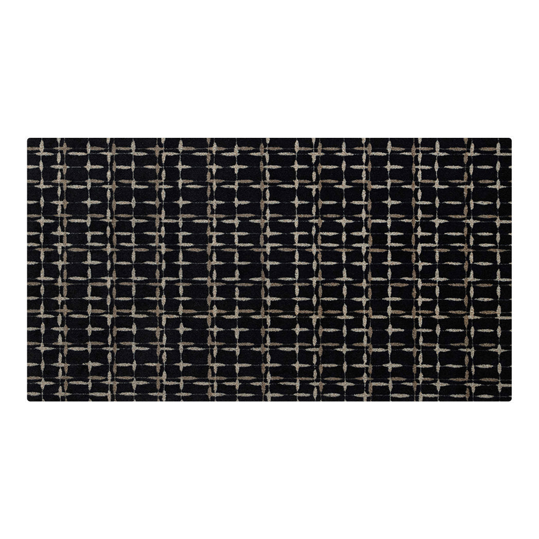 Maxcent Heritage Tweed area mat in Inkwell, medium size – features a black background with a crosshatch pattern in light gray and tan, creating a woven grid effect. The carpeted surface adds softness underfoot, and the non-slip rubber backing ensures secure placement on hard flooring.