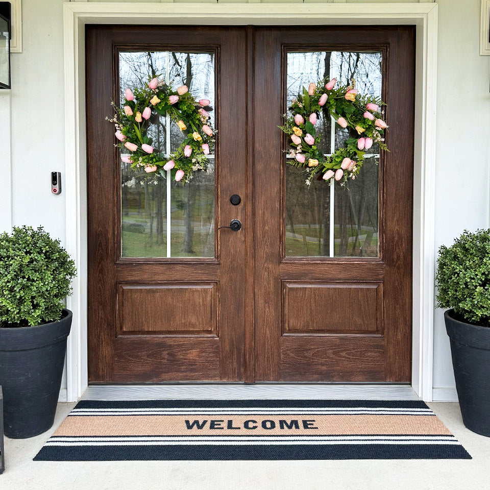 Low-profile, non-shedding Modern Moniker double door entrance mat personalized with welcome, in front of two beautiful dark oak doors.