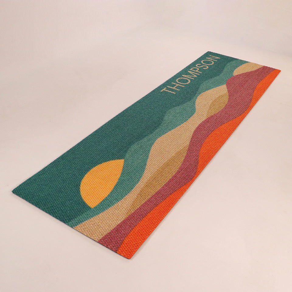 Angled left, double-door size image of Personal Sunset mat personalized with street address numbers and vibrant colors of aquas, coir, maroon, electric orange, and a yellow setting sun.
