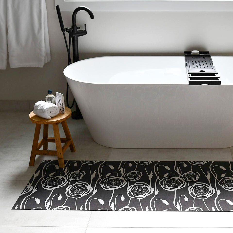 Low-profile Un-Rug featuring a modern floral pattern in dark grey is placed in front of a bathtub to provide traction.