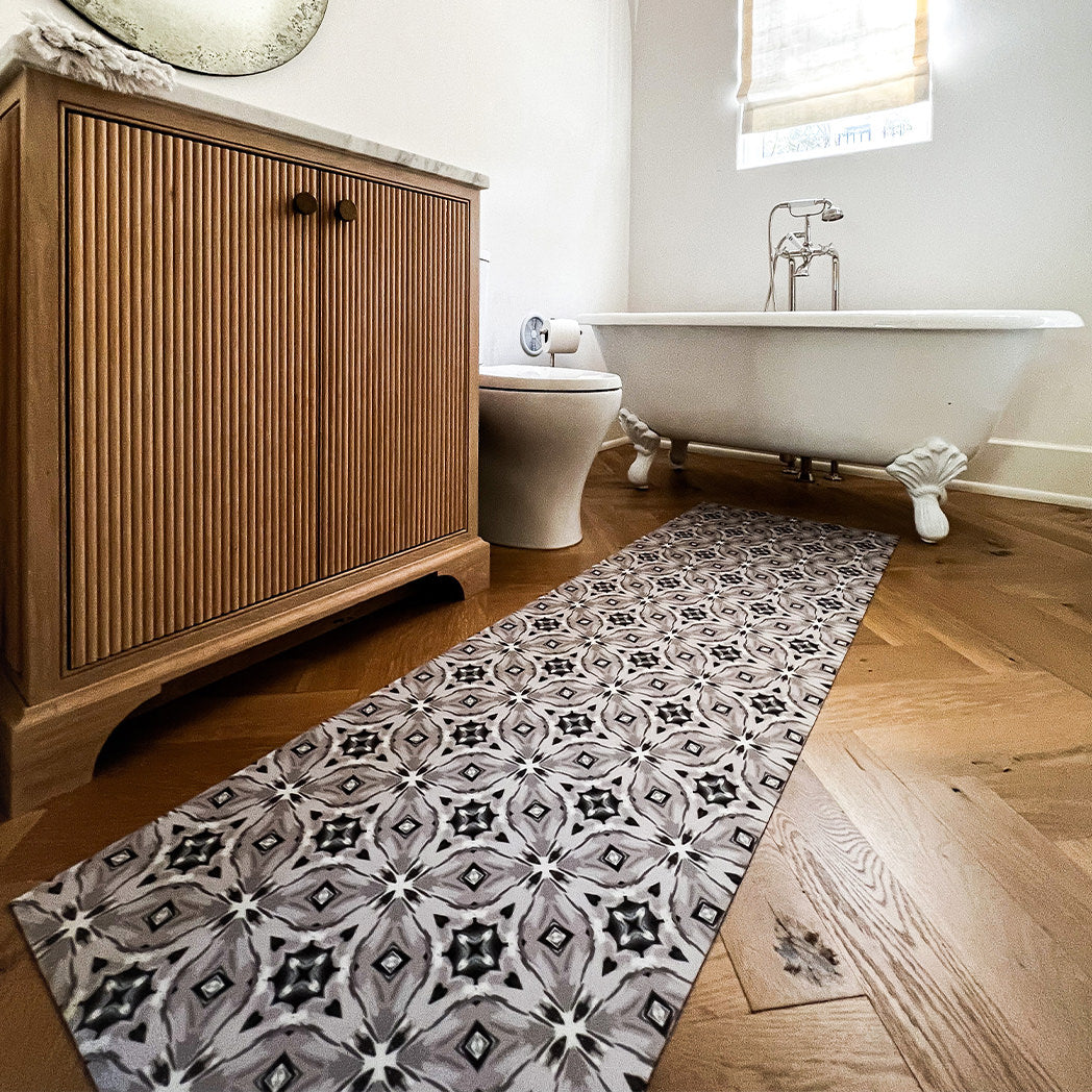 Decorative Un-Rug floor mat show in a runner size is placed in front of a single sink vanity and adjacent toilet while also serving as a walk out mat for the bathtub.