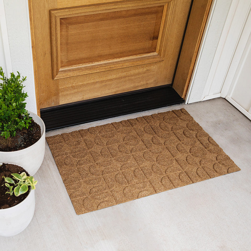 A WaterHog Luxe all-weather, low-profile mat in the color wheat located at the entrance of a home.