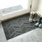 WaterHog Luxe shown in chevron pattern in dark grey color is placed inside at a back door with dirty shoes on top.