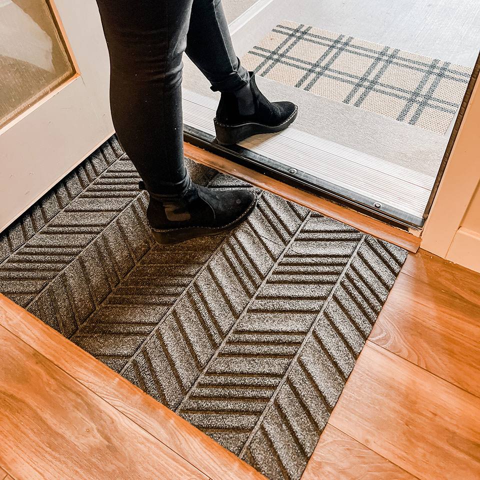 Chevron single door doormat shown in greige on inside of door paired with classic tan black plaid doormat.