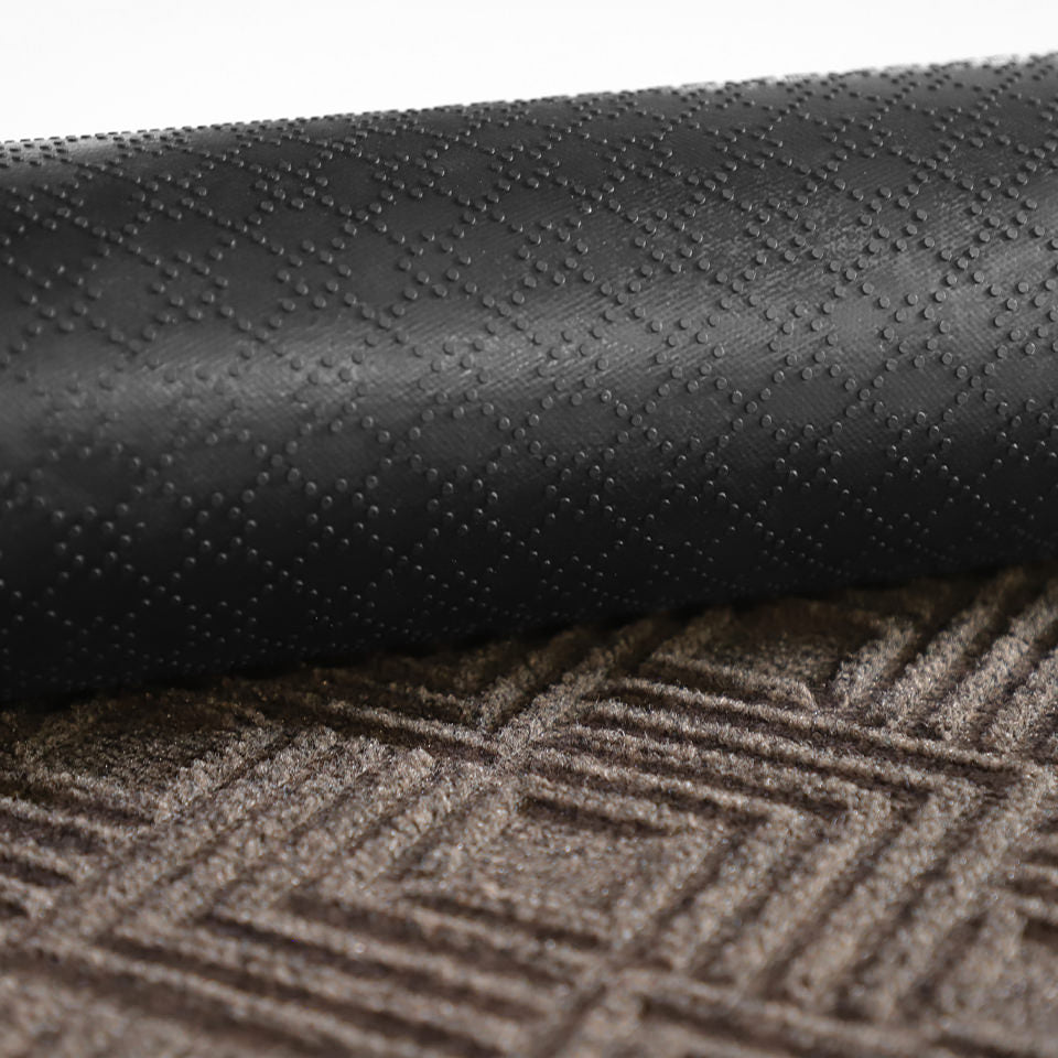 A close-up image of the all-weather Labyrinth mat half rolled showing both the rubber backing and greige surface.