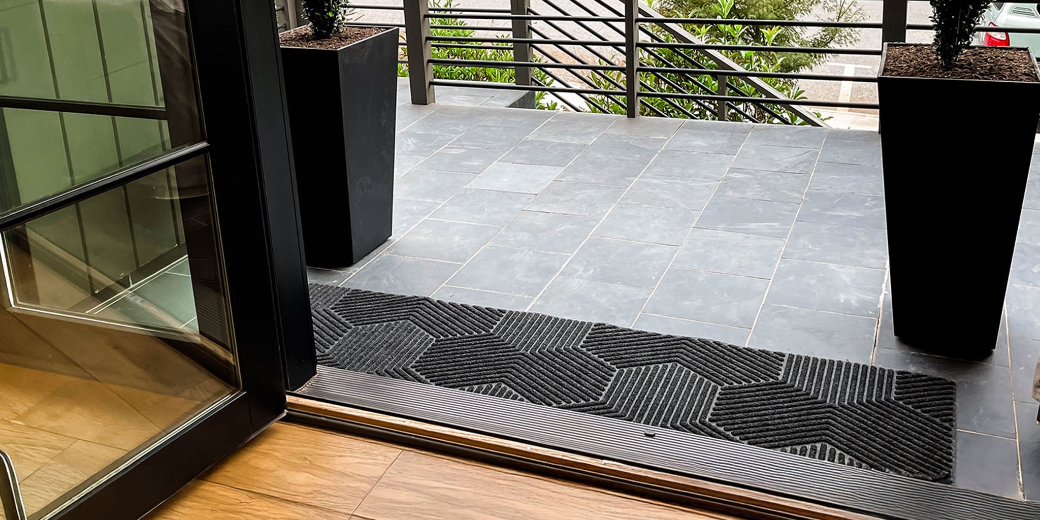 Large WaterHog Luxe Double Door Doormat placed at the front of a modern home with large glass paned double doors.