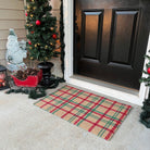 Front door with a red and green indoor/outdoor plaid doormat, Christmas decorations, and a small tree.