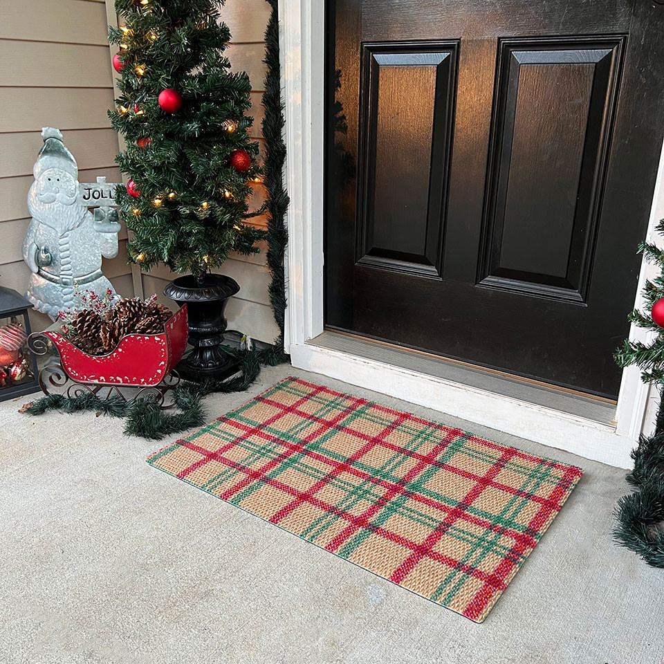 Front door with a red and green indoor/outdoor plaid doormat, Christmas decorations, and a small tree.