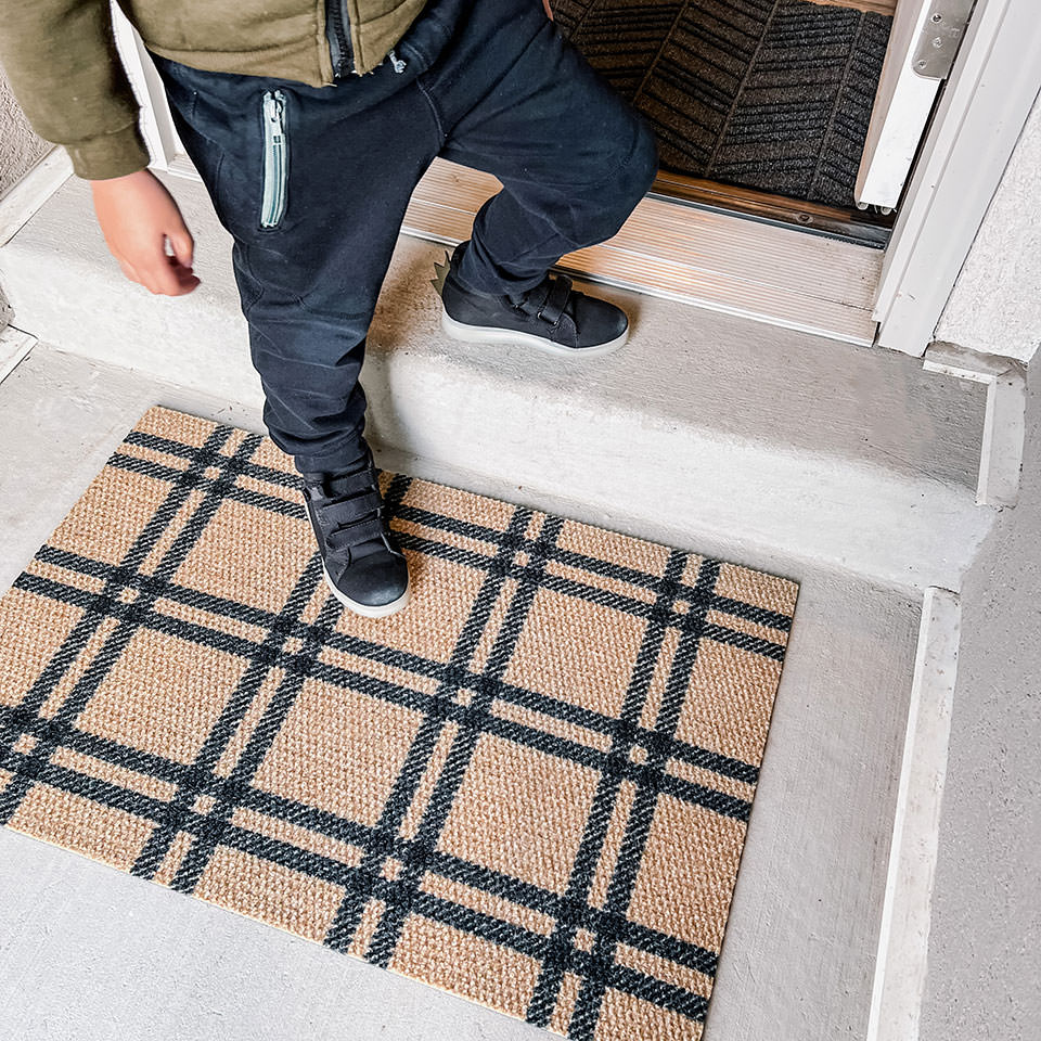 single door size coir and black classic plaid doormat placed by front door