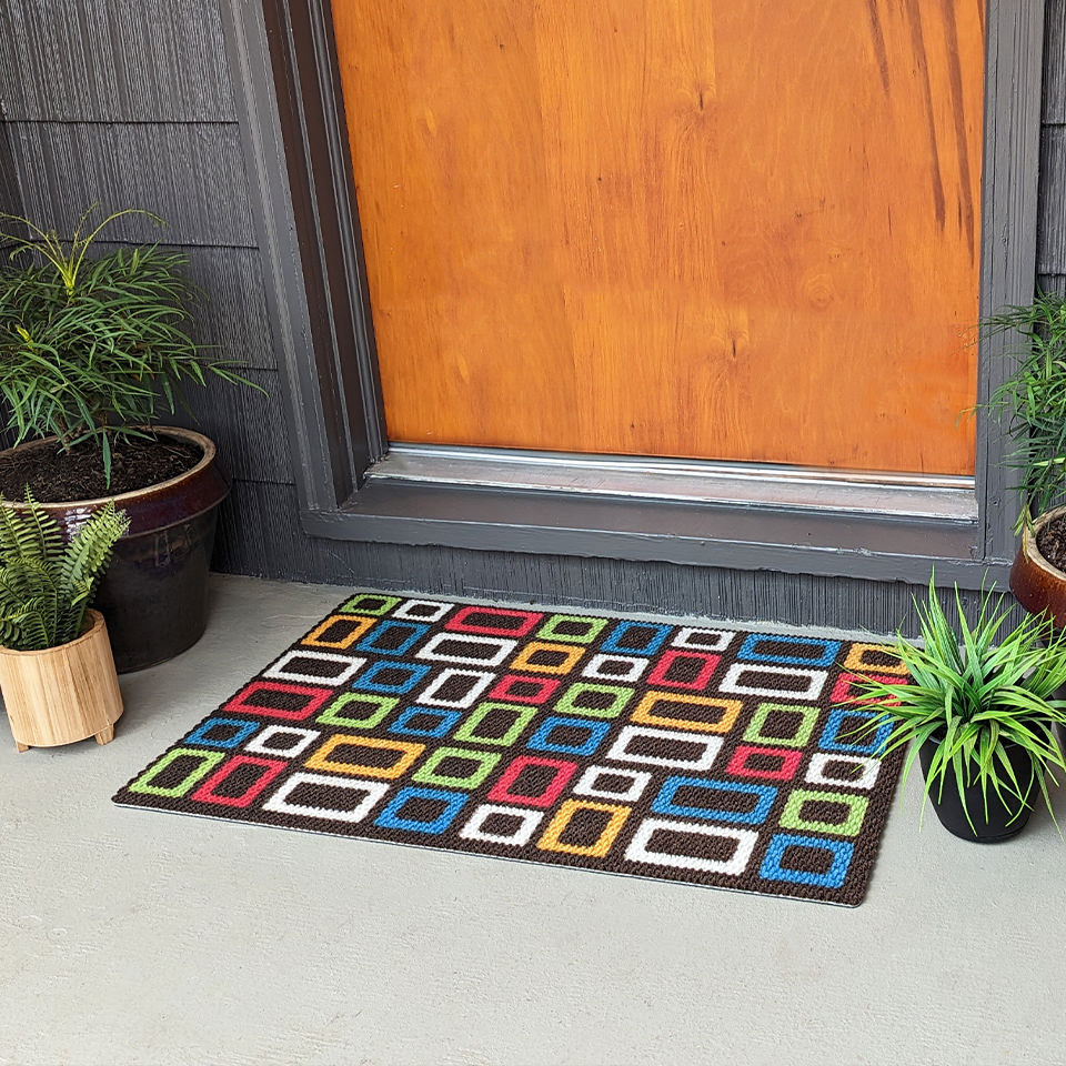 Multi colored retro squares on a dark brown doormat in front of a covered front porch