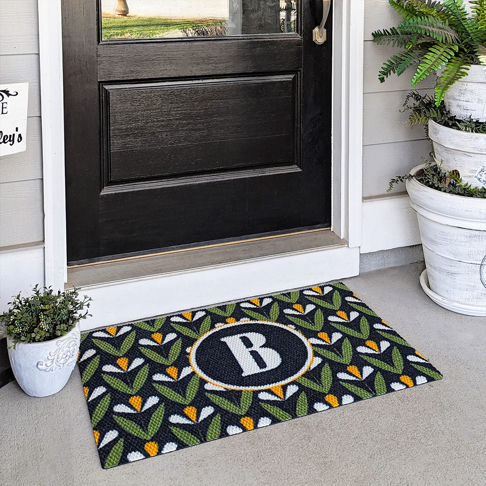 Spring Blooms monogrammed doormat in green, yellow and black shown on a covered porch by the front door.