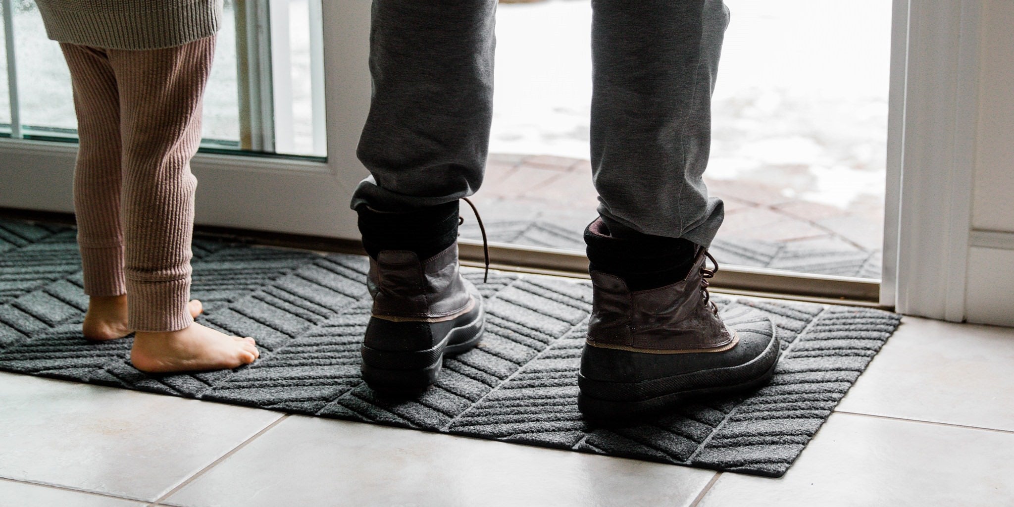 Small child standing on durable all-weather WaterHog outdoor doormat placed at sliding door to capture snow.