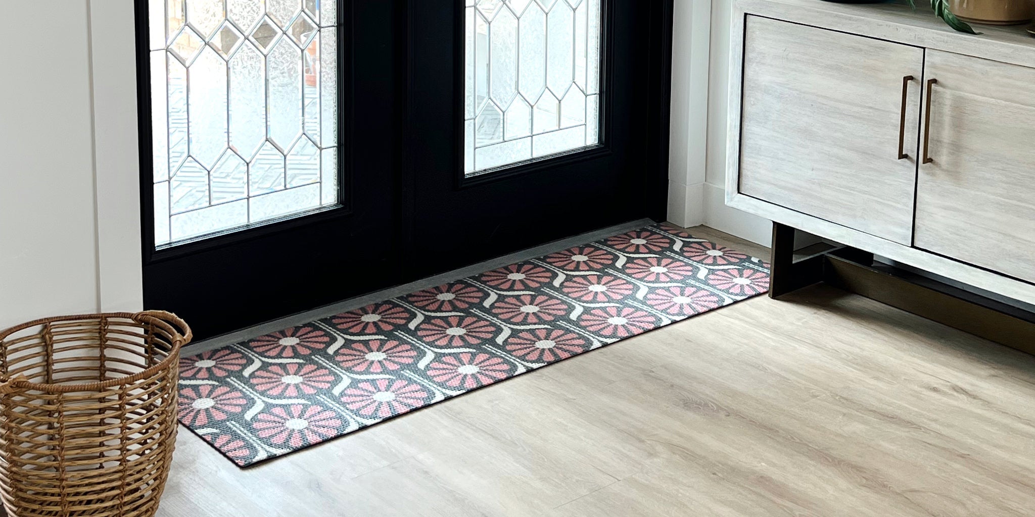 Matterly front door doormat featuring a modern floral design in colors of red, black and white. This welcome mat is placed on a covered black and white checkered pattered wood deck and flanked by a potted plant.