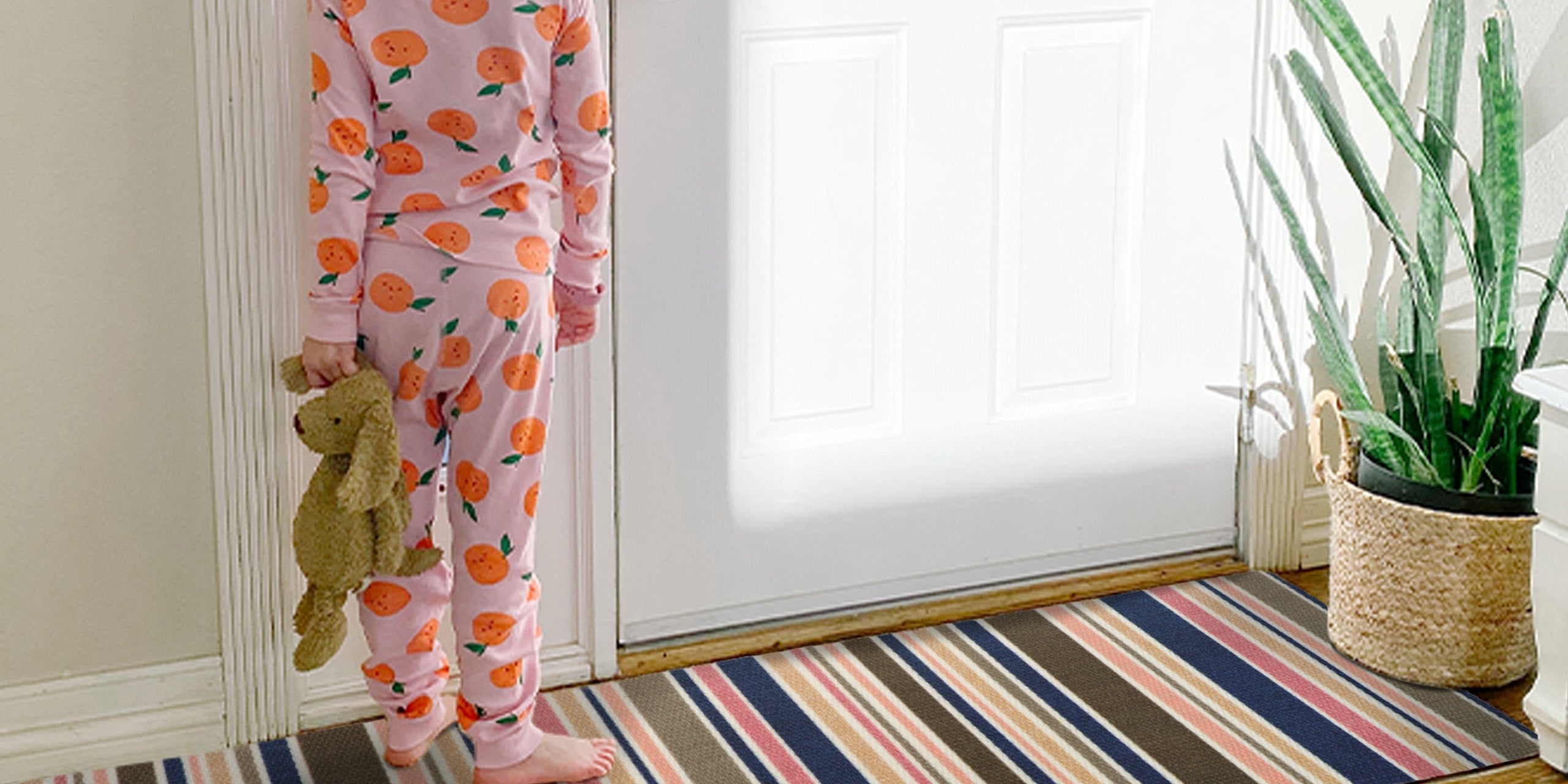 Little girl holding a stuff animal standing on a double door Neighburly Everly Stripes door mat.