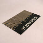 Angled shot of Fall in Line personalized single-sized doormat featuring a last name in white on a black and coir design.