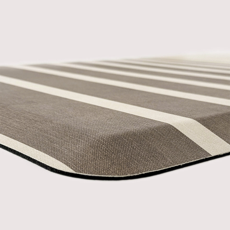 Corner of Happy Feet anti-fatigue mat with dark beige/light brown stripes with a canvas-like texture. 