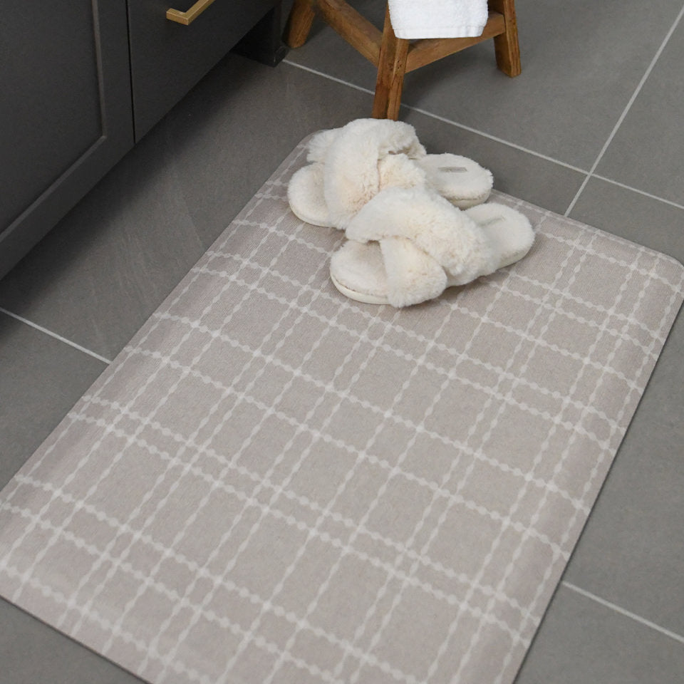 A small Beaded Plaid anti-fatigue comfort mat in a grey colored bathroom with white slippers on top