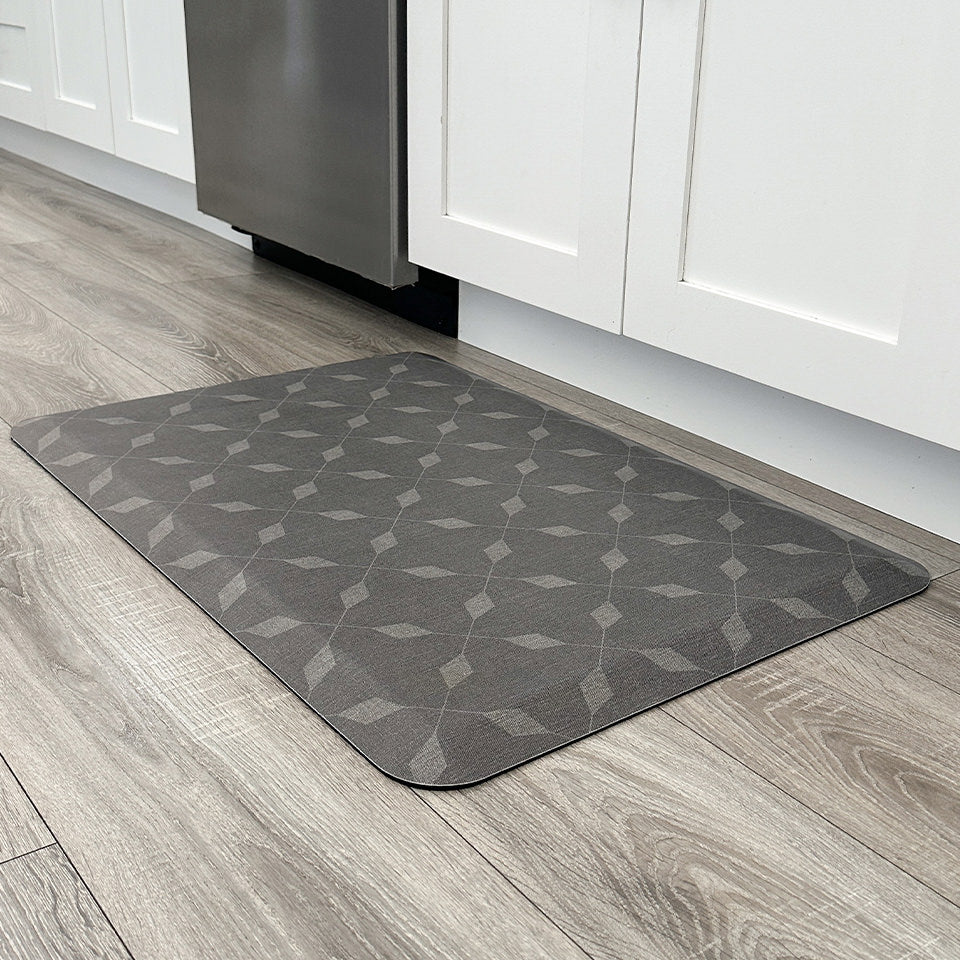 Crossing Paths comfort mat in a kitchen with grey wood floors and white cabinets