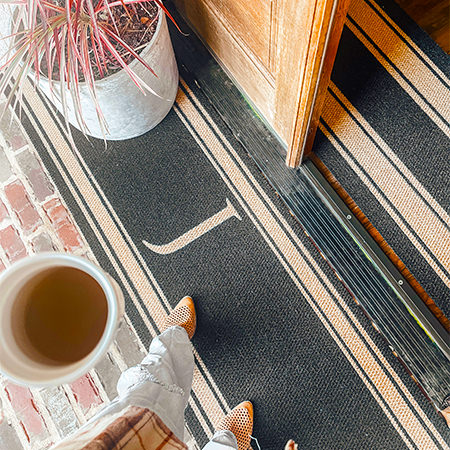 Matterly Initial Stripes doormat features the letter of your choosing placed in the middle of the mat. Door mat shown is a double door mat placed just outside of a front door on a brick surface.