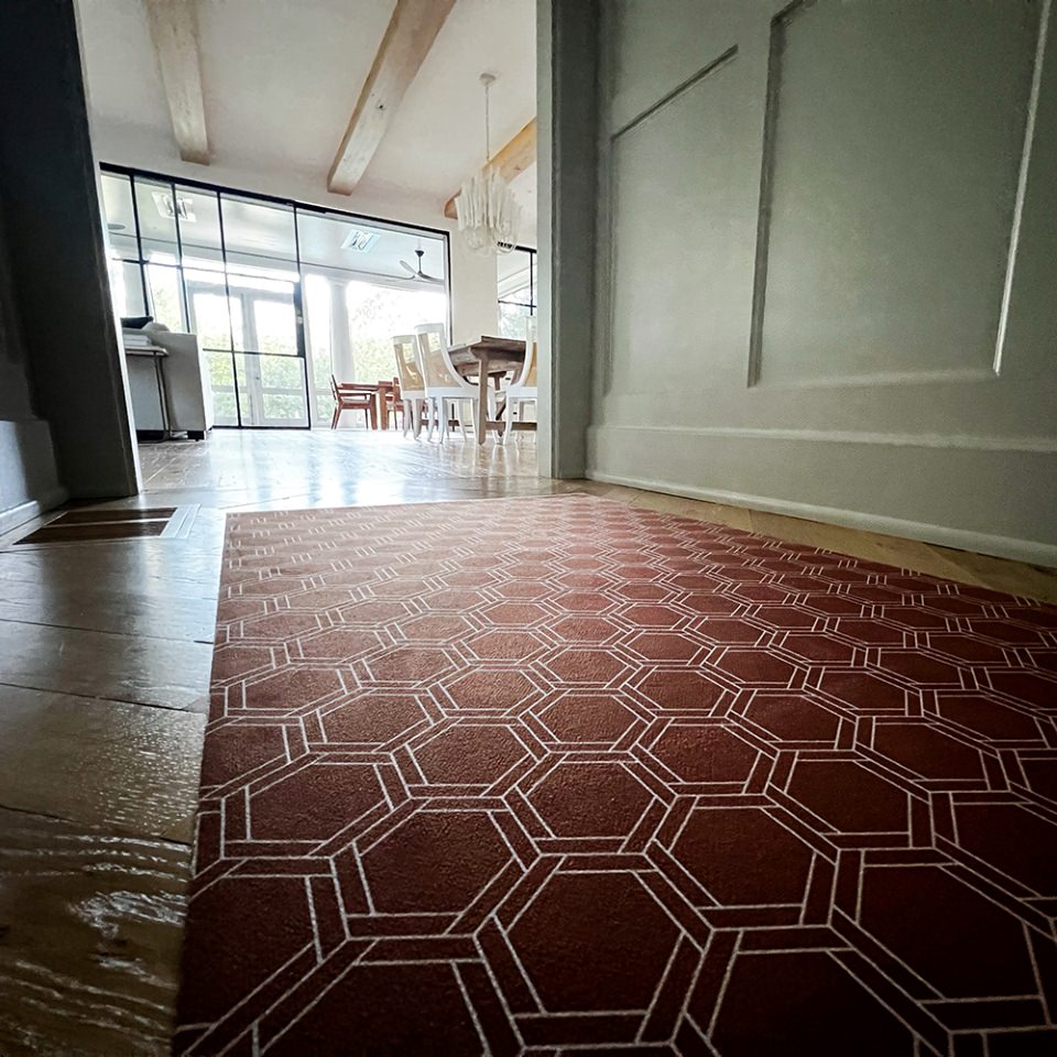 Low profile washable floor mat in burnt orange linen look with double honeycomb accent design in shiitake tan boasts a durable rubber backing and is shown being used as a hallway runner.
