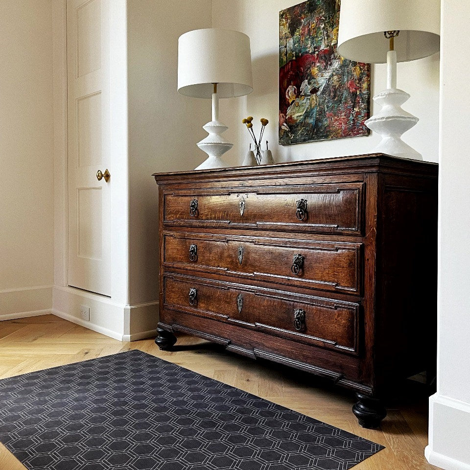 Un-Rug in Urbane Bronze features a brownish linen look with double honeycomb accent design in shiitake tan printed on a low profile washable indoor floor mat placed in front of a bedroom dresser.