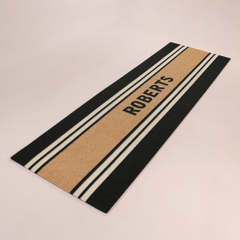 Angled double door Modern Moniker mat personalized with a last name on a coir stripe with multiple stripes on black background.