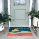 Colorful, low-profile doormat personalized with the last name Parkison along the top with an abstract sunrise below.