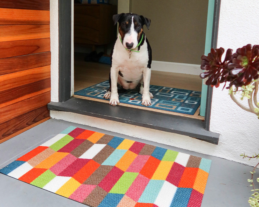 Neighburly Colorful Tulips low-profile entrance mat with a geometric design of bright reds, browns, blues, greens, yellows, and oranges.